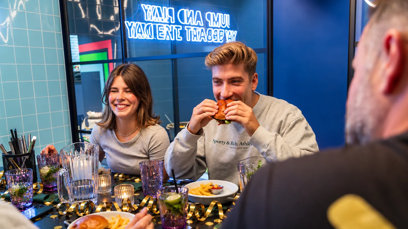 Junge Erwachsene essen Burger an einem gedeckten Tisch