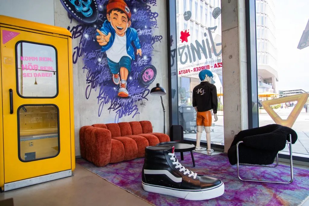 Sitzecke mit gelber Telefonzelle, rotem Sofa und Kibu-Jumper-Wandbild